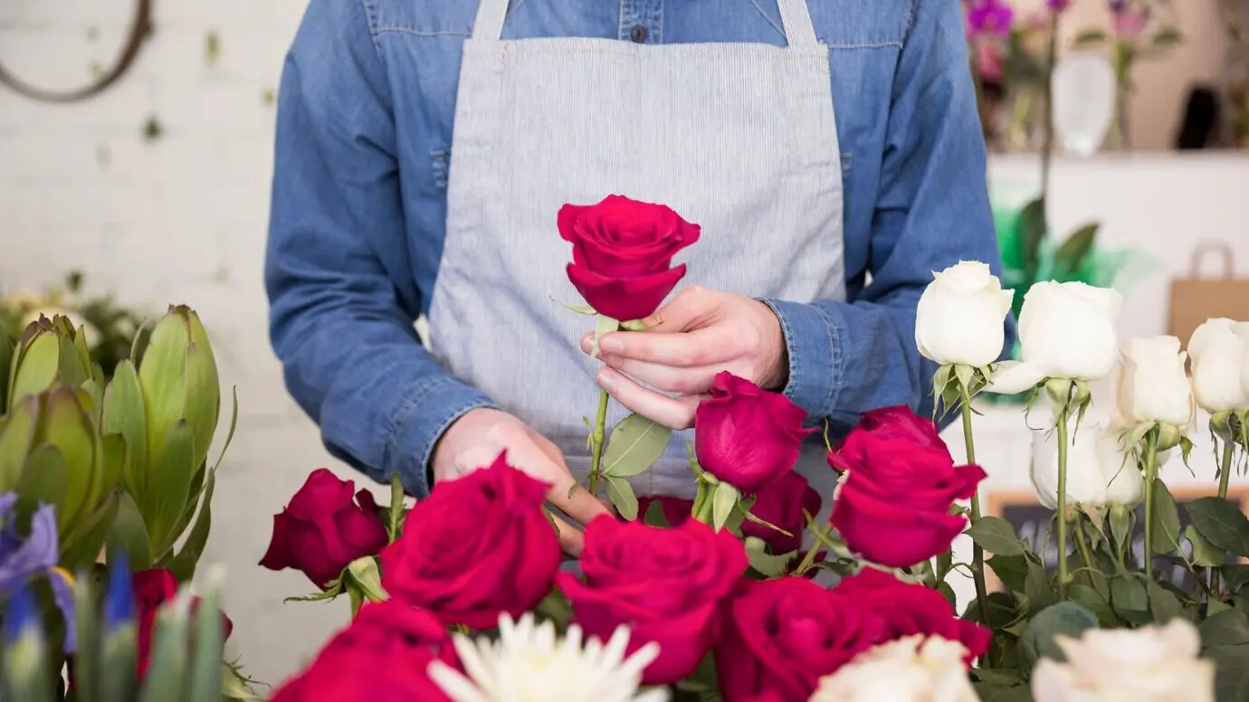 Ausschnitt der Körpermitte eines männlichen Floristen, der die Rose im Blumenstrauß arrangiert.