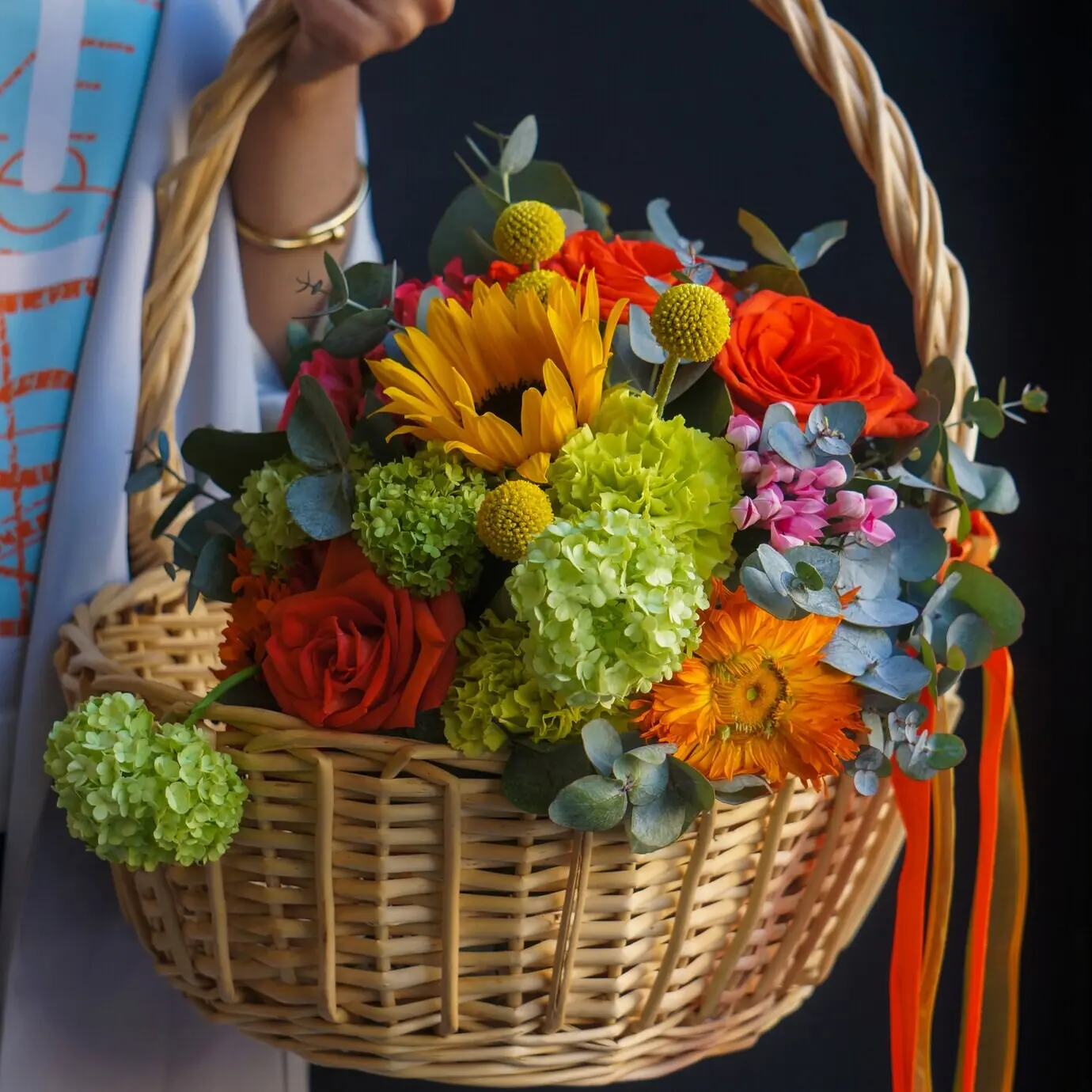 Ein Bambuskorb mit Sonnenblumen, roten Rosen und Nelken.
