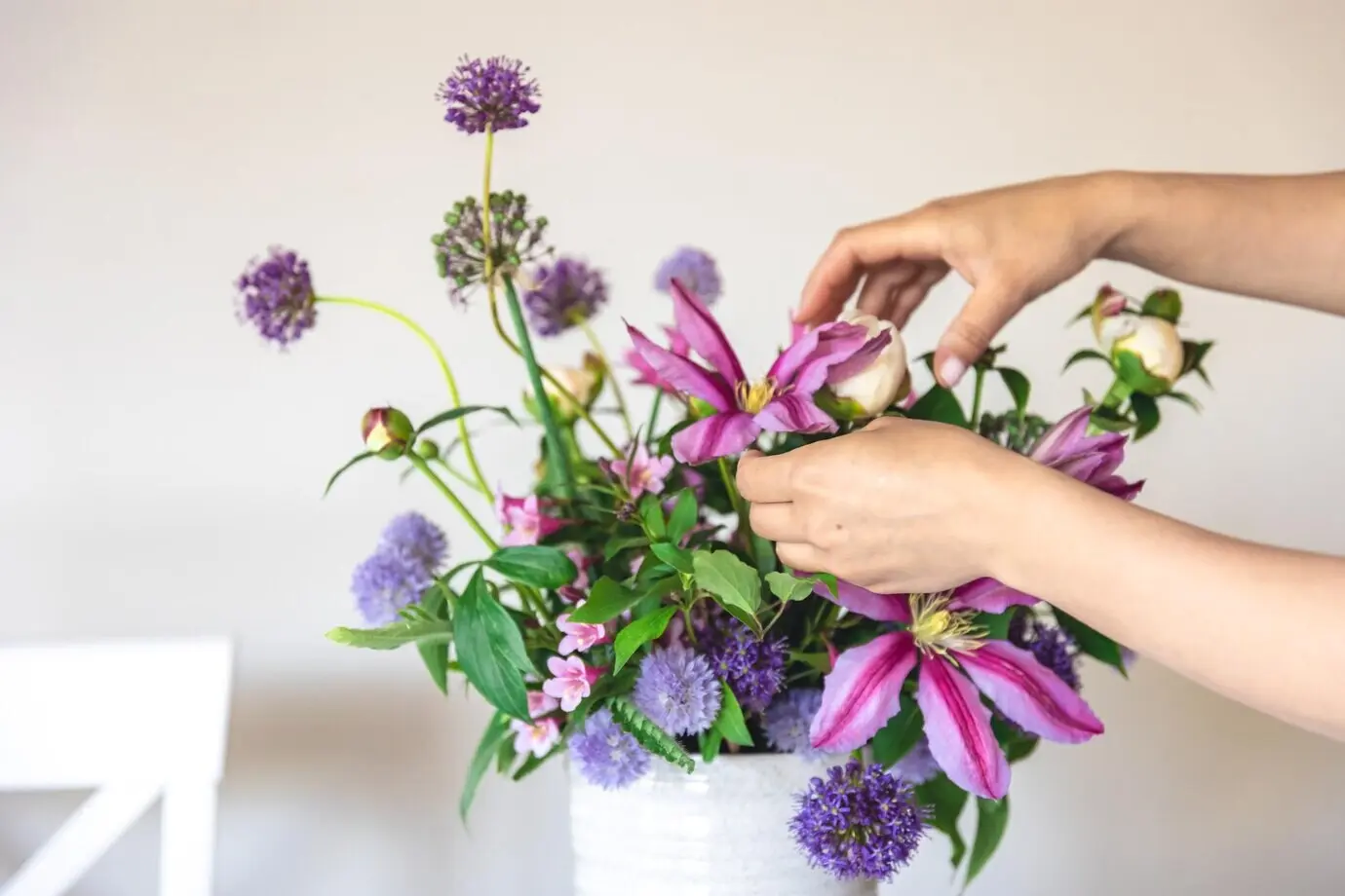 Vase mit frischen Sommerblumen in weiblichen Händen vor weißem Hintergrund